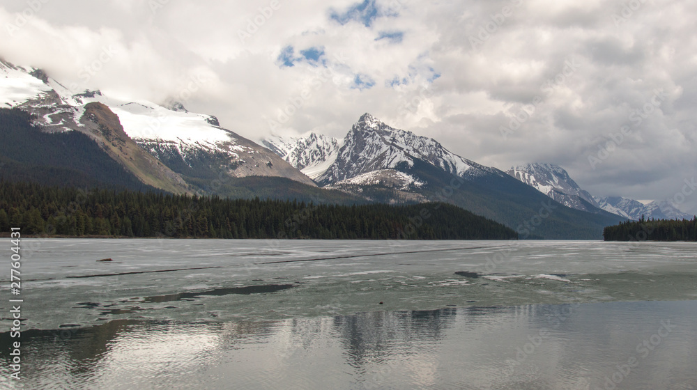Cloudy Rocky mountains in British Columbia reflecting in the icy water