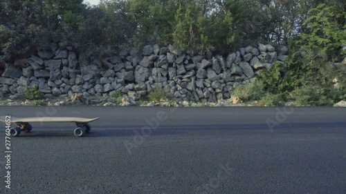 Slow motion video of an unrecognizable young skateboarder jumping on a moving skateboard. Still shot, actor moving from left to right.