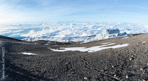 Footprints lead off through volcanic ash and dust towards a glacier sitting above the clouds on the summit of Mount Kilimanjaro, Tanzania, near the Uhuru Peak on a bright morning just after sunrise. photo