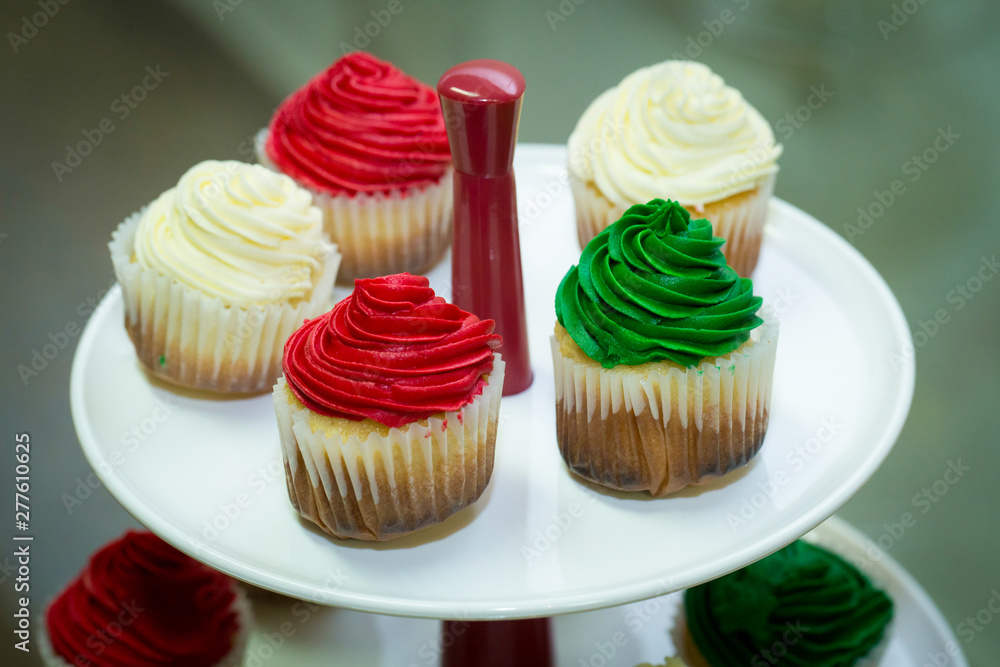 Unhealthy food concept. Isolated green, white and red cupcakes on a white tray. Tasty sweet desserts. Party background.