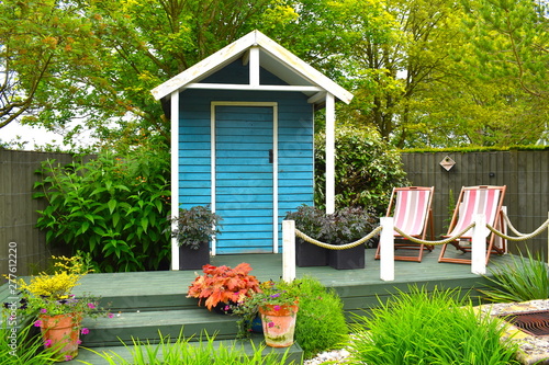 Wooden blue painted garden tools storage shed among green grass, potted plants and pink deckchairs in summer in the English countryside. Northamptonshire, UK photo