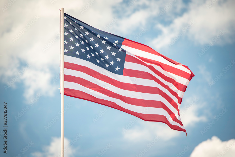 Naklejka premium An American flag fluttering in the wind against a blue sky with clouds.