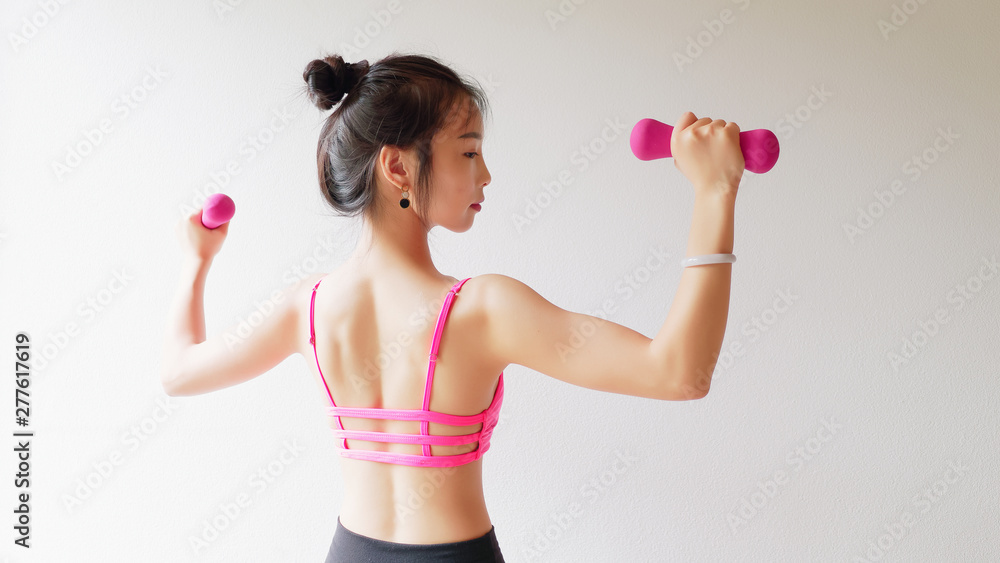 Bodybuilding. Strong fit woman exercising with dumbbells. Muscular Asian girl in pink sexy sportswear lifting weights and doing exercise for arms, back view studio shot on white background. Bodybuilding. Strong fit woman exercising with dumbbells. Muscular Asian girl in pink sexy sportswear lifting weights and doing exercise for arms, back view studio shot on white background.