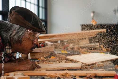 senior carpenter blowing wood dust in making woodwork for hobby