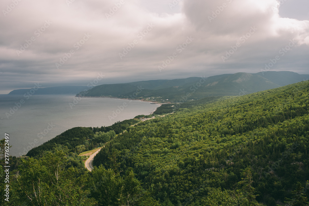 A winding paved road through the evergreen forests on the coast the Cabot Trail in Cape Breton Nova Scotia just outside Cheticamp with clouds and sunlight visible