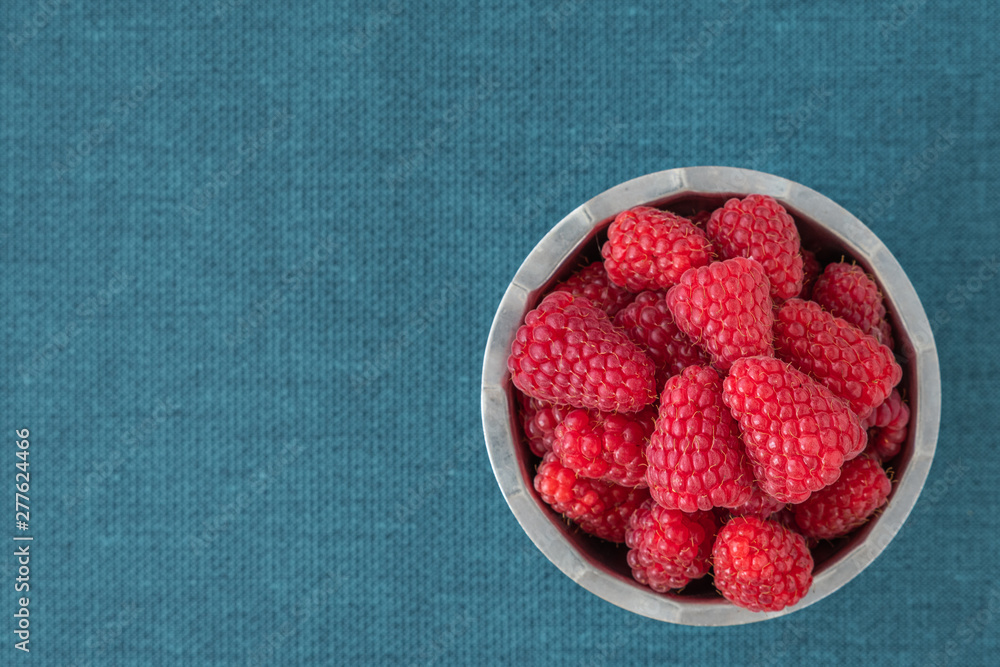 Bowl of fresh red raspberries for dessert, stainless steel bowl, blue fabric background Bowl of fresh red raspberries for dessert, stainless steel bowl, blue fabric background