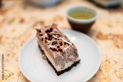 Macro closeup of chocolate coconut tiramisu vanilla cheesecake bar dessert raw vegan dessert on white plate with cacao nibs topping and green tea