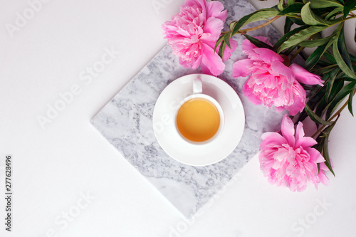 Fashion blogger styled desk frame with flowers, cup of herbal tea, pink peonies on marble plate on white, breakfast morning lifestyle, minimal concept, copy space