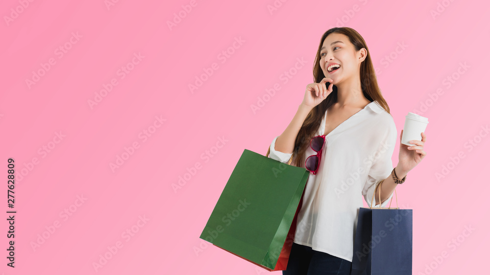 Asian beautiful women blogger are hand guesturing and holding coffee cup with shopping bag in pink color background.Concept of lifestyle shopping business.