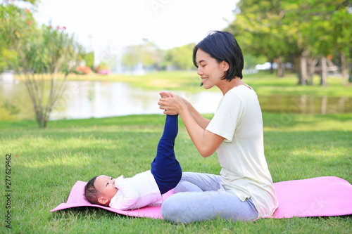 Portrait of Asian mother doing baby yoga for her son on green lawn in the nature garden outdoor.
