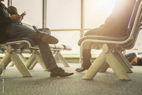 travelers are sitting at airport terminal for flight departure, close up on legs and using mobile action in warm sunlight from glass window photo