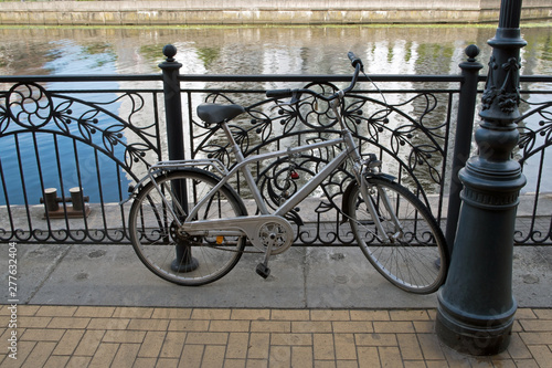 Gray bike parked and attached to the fence of the river embankment