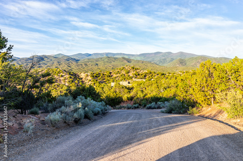 Sunset Santa Fe, New Mexico mountains in Tesuque with golden hour light on green plants and dirt road to residential community photo