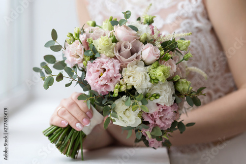 The bride holds a wedding bouquet in her hand against the background of a white dress. Bridal bouquet on the wedding day. Flowers for the bride. A small bridal bouquet close-up.