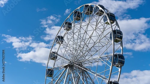 Timelapse Ferris wheel rotates on the background of passing clouds in the blue sky. Time lapse children's amusement ferris wheel sunny summer day. photo