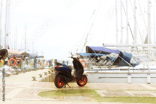 Scooter stands on the dock on the background of sailing cruise yachts in the Mediterranean marina. Popular transport of yachtsmen and maintenance personnel of the marina. Prestigious lifestyle