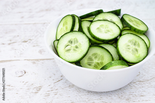 Sliced rings of green cucumbers in a white plate on a white background.