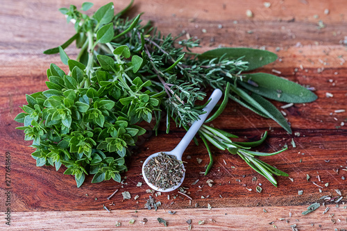 Ceramic spoon with dried herbs and fresh thyme, sage and oregano on wooden plate