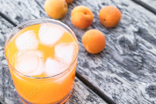 Fresh apricot juice with apricots and ice cubes in a glass against the background of old boards. Summer soft drinks.