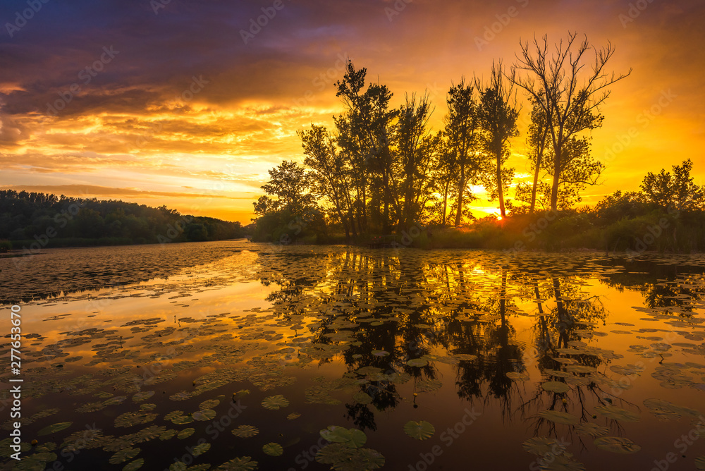 Scenic river in early summer with sun on the sunset time. Calm water with reflections of colorful clouds. Hungary