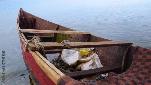 Small wooden red fishing boat lies in still water by the shore of African lake. photo