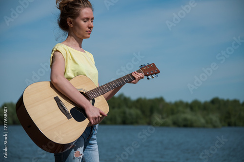 beautiful young woman with close eyes standting on beach with guitar, sunny day photo