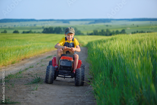 Little boy farmer on a tractor among green grain fields