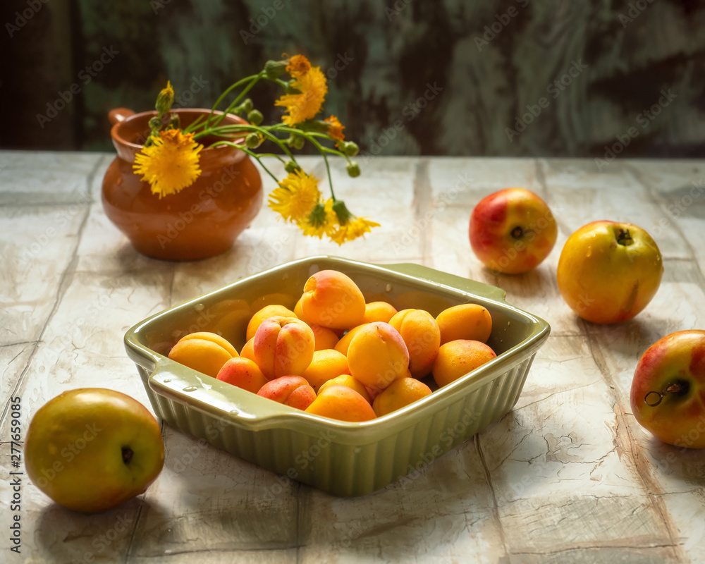 Ripe apricots in a green ceramic on a wooden table, a small bouquet of flowers MOTHER-AND-MACHEA
