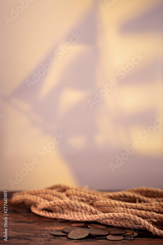 Ship silhouette as a background, rope and old coins on oak table. Pirates style. photo