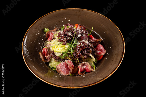 Plate of roast beef salad  with fresh tomatoes, salad mix with ginger sauce and parmesan cheese isolated at black background.