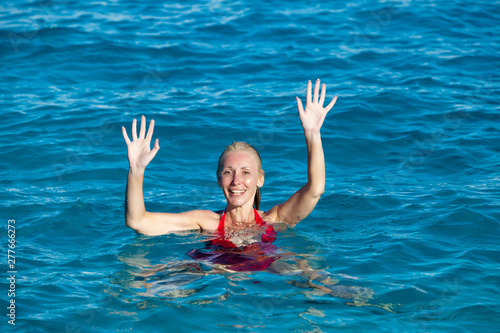 The young woman in a red bathing suit on sea background greeting waving..