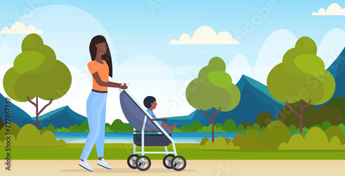 mother with toddler son in stroller walking outdoor african american woman pushing pram with child happy family motherhood concept urban city park landscape background full length horizontal