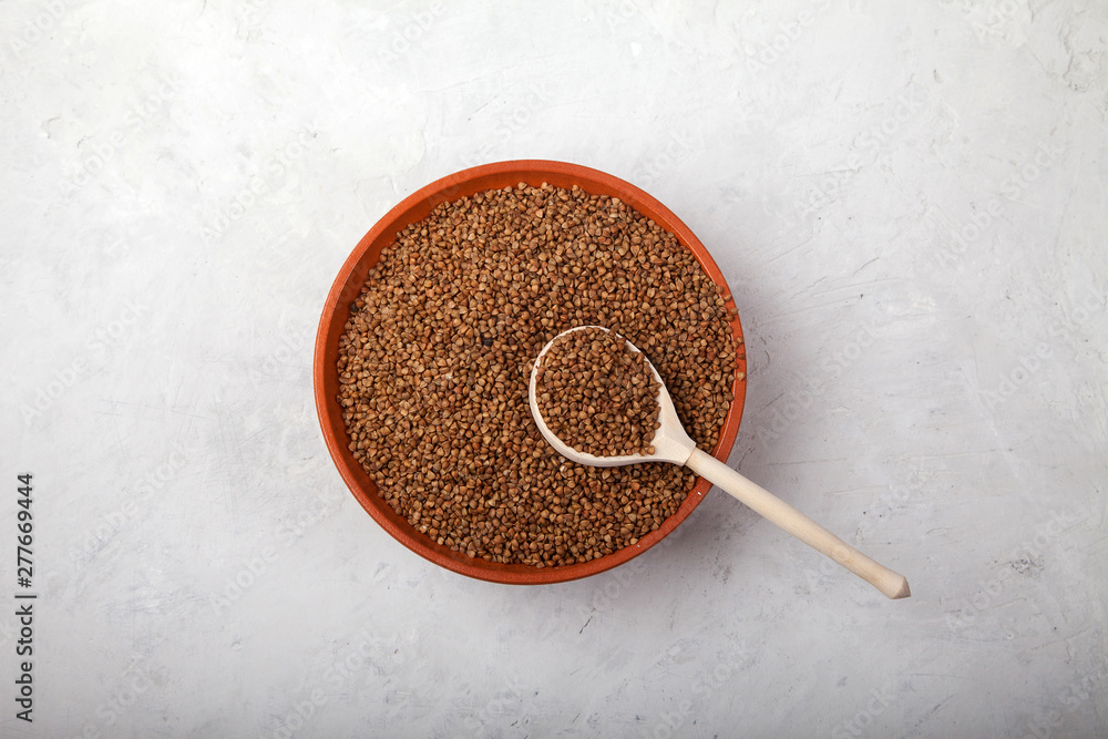 buckwheat with a wooden spoon in a clay bowl on a white background. superfood buckwheat with a wooden spoon in a clay bowl on a white background. superfood