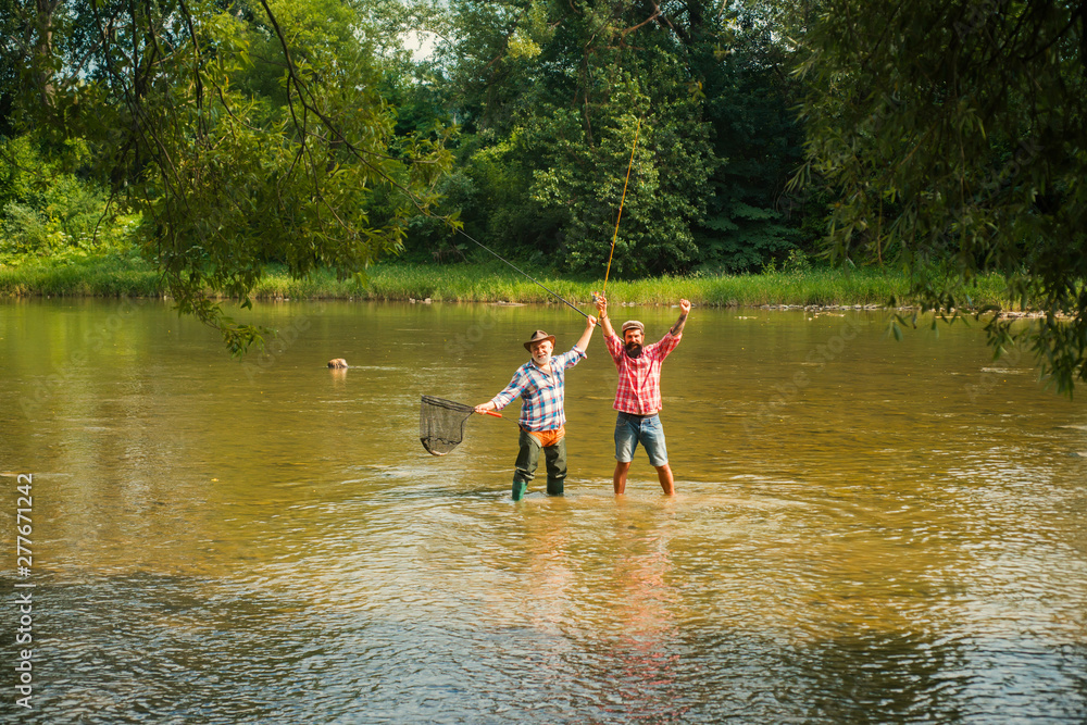 Generations ages: grandfather and father. Fisherman fishing in a river with a fishing rod. Still water trout fishing. Family and generation - summer holidays and people concept. Generations ages: grandfather and father. Fisherman fishing in a river with a fishing rod. Still water trout fishing. Family and generation - summer holidays and people concept.