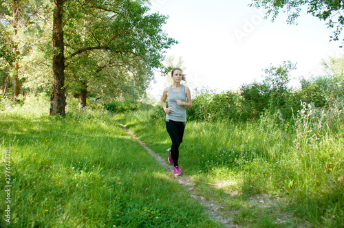 Beautiful  athletic  slender woman with headphones and sports suit runs through the park  summer  sunny morning. Morning jogging and sports