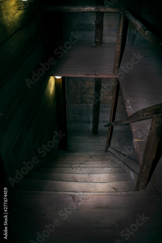Darkness and horror in a ghostly building. Inside on a dark wooden staircase with steps down to the basement of an old abandoned house with black walls mystical light from a dim lamp on the floor