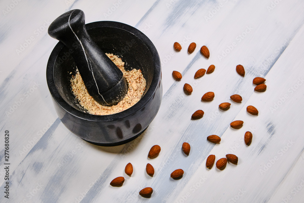 Fototapeta premium Almonds for cooking on a wooden white background. Grinding nuts in a mortar. Preparation of almond flour, top view.