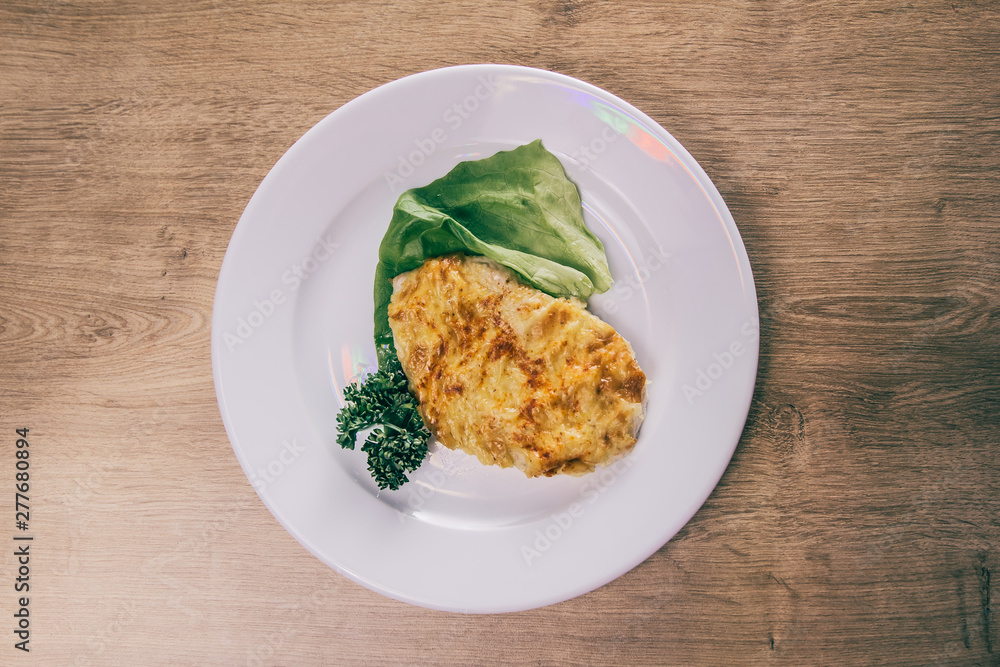 chicken fillet in cheese and lettuce on a white plate chicken fillet in cheese and lettuce on a white plate
