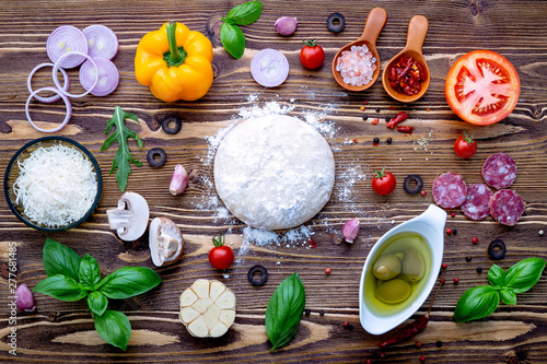 Raw dough with ingredients for homemade pizza on shabby wooden background.