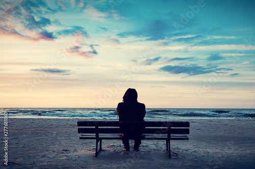 Valokuvatapetti Man in hood sitting on a lonely bench on the beach