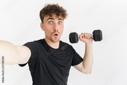 Photo closeup of attractive sporty man in t-shirt looking at camera and taking selfie photo while holding dumbbell