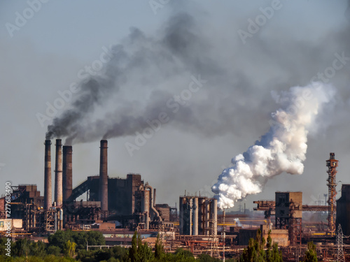 Air pollutants emissions - high amount. Toxic smoke of air pollutants, released into the atmosphere by chimney smoking stack at by-product coke plant in metallurgy industry.