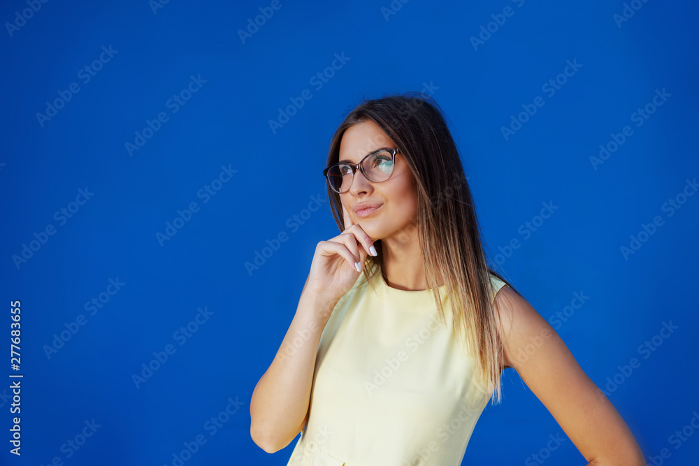 Portrait of beautiful pensive Caucasian teenage girl in yellow dress standing in front of blue background. Portrait of beautiful pensive Caucasian teenage girl in yellow dress standing in front of blue background.