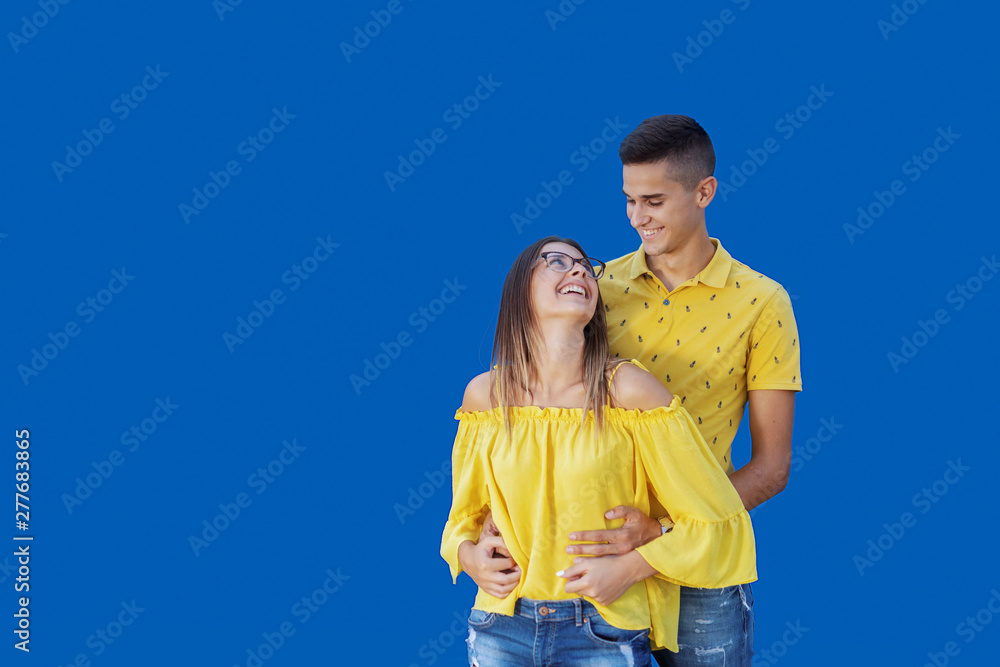 Cute happy Caucasian couple in blue and yellow outfit hugging and posing in front of blue background. Cute happy Caucasian couple in blue and yellow outfit hugging and posing in front of blue background.