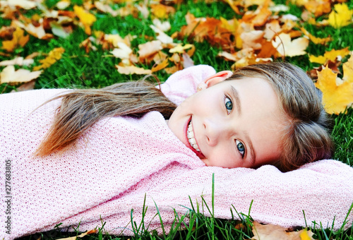 Fotografi Autumn portrait of adorable smiling  little girl child lying in leaves
