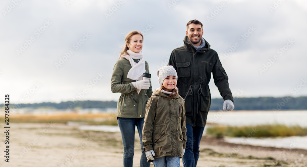 family, leisure and people concept - happy mother, father and little daughter walking along autumn beach