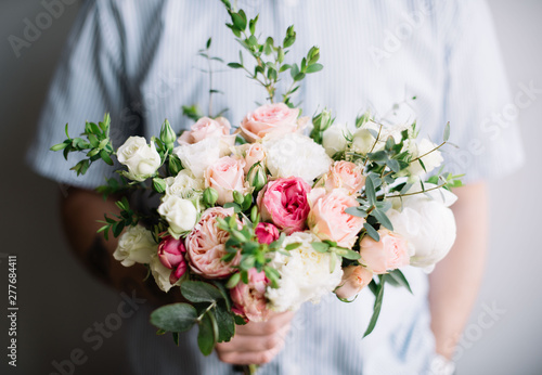 very nice young man in a shirt holding a beautiful blossoming flower wedding bouquet of fresh peonies, roses, in pastel white and pink colours on the grey wall background