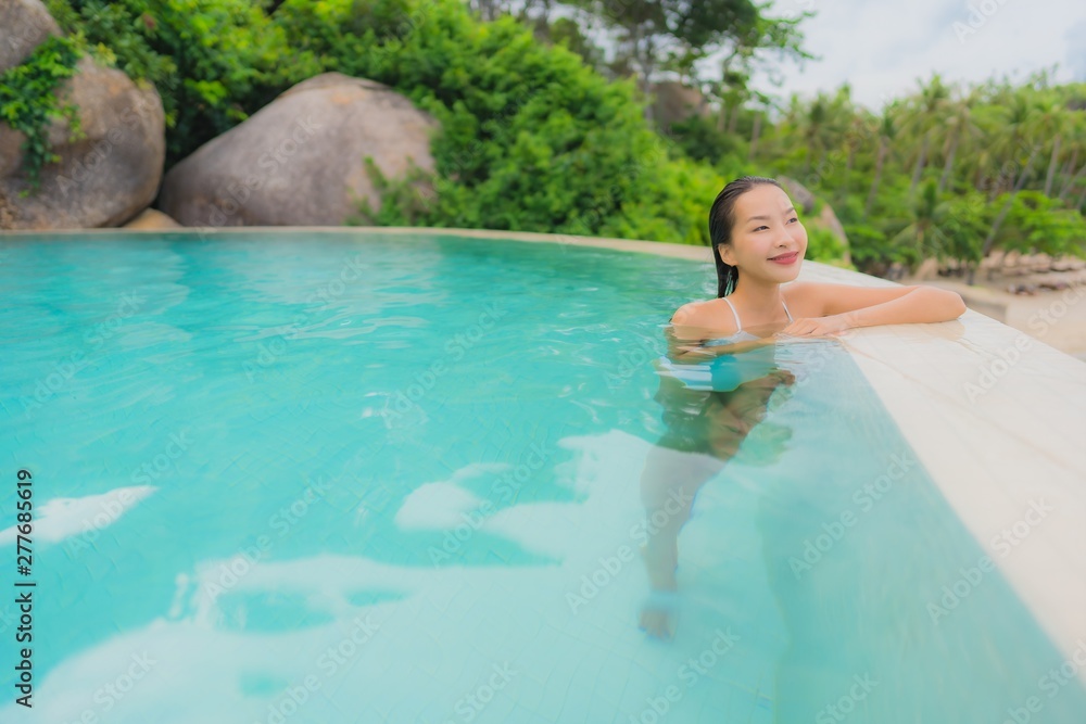 Portrait young asian woman relax smile happy around outdoor swimming pool in hotel resort with sea ocean view