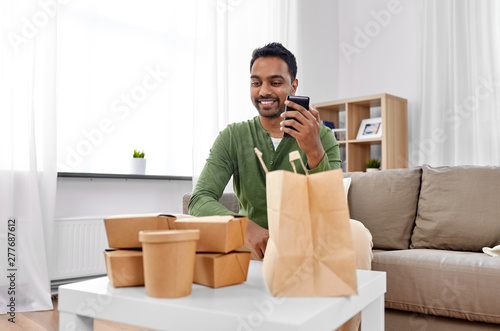 communication, leisure and people concept - indian man using smartphone for takeaway food order check up at home