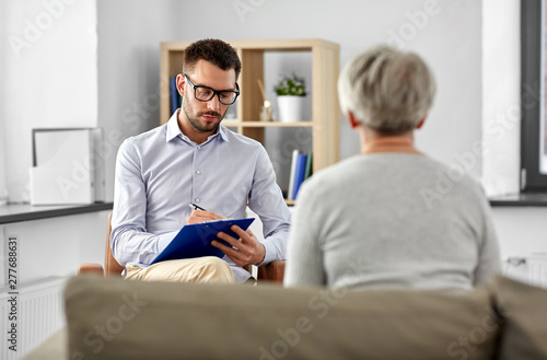 geriatric psychology, mental therapy and old age concept - senior woman patient and psychologist with clipboard taking notes at psychotherapy session photo